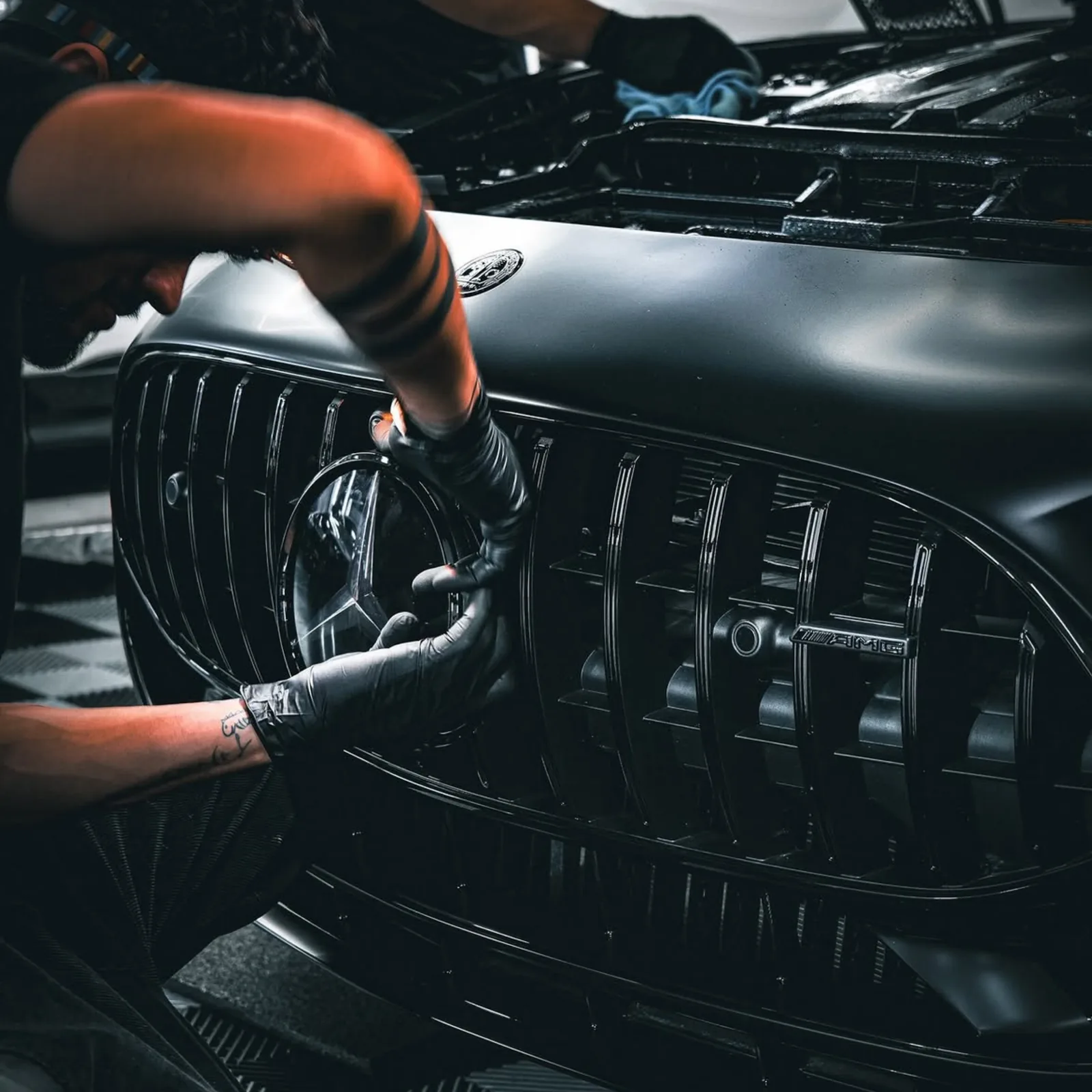 Gloved hands cleaning between the slats of a Mercedes grille